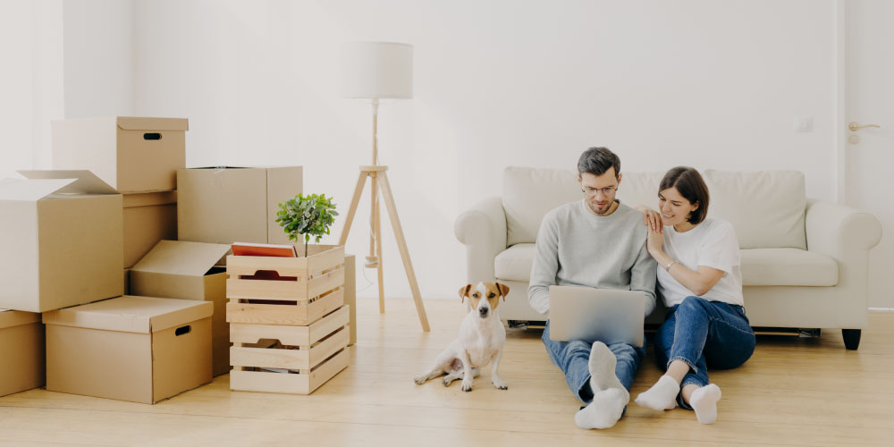 Pärchen und Hund sitzen mit Laptop auf dem Boden