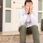 Ein Mann trennt sich von seiner Frau und sitzt vor der Tür vom gemeinsamen Haus, die Scheidung steht bevor