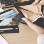 Eine Frau blickt in eine leere Geldbörse, was tun bei einem finanziellen Engpass?