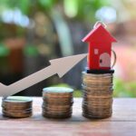 Modell mit einem Haus, Münzen und einem Pfeil, wie entwickeln sich die Immobilienpreise?