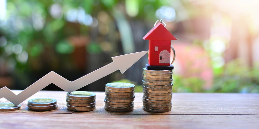 Modell mit einem Haus, Münzen und einem Pfeil, wie entwickeln sich die Immobilienpreise?