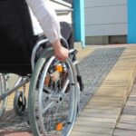 Ein Mensch fährt mit einem Rollstuhl eine Rampe hinauf, ein Beispiel für barrierefreies Bauen