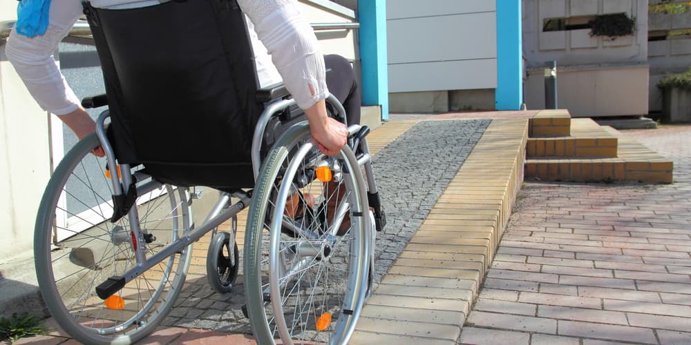 Ein Mensch fährt mit einem Rollstuhl eine Rampe hinauf, ein Beispiel für barrierefreies Bauen