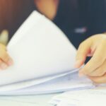 Eine Frau sucht in einem Papierstapel nach dem ESIS Merkblatt