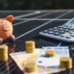 Sparschwein, Geld und Taschenrechner auf einem Solarpanel als Symbol für die Photovoltaik-Finanzierung