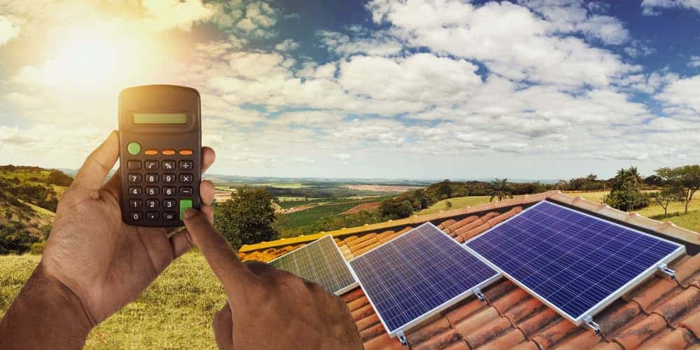 Solarpanels auf einem Dach und ein Taschenrechner, wie funktioniert die Photovoltaik-Finanzierung?